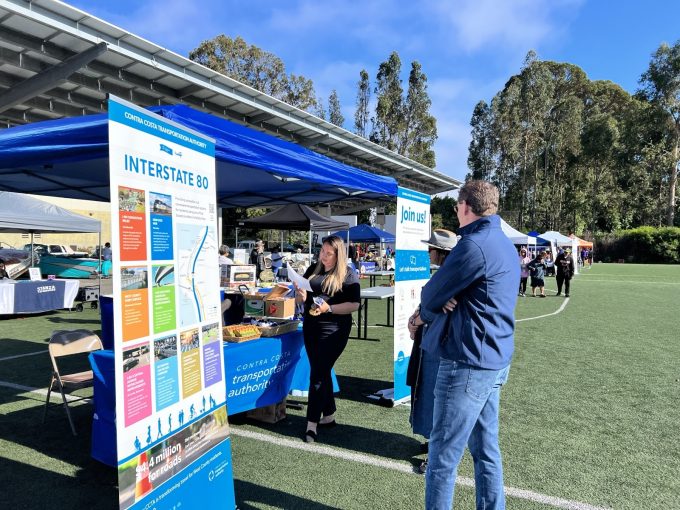 People at an outdoor event booth of the Contra Costa Transportation Authority, with informational displays about Interstate 80.