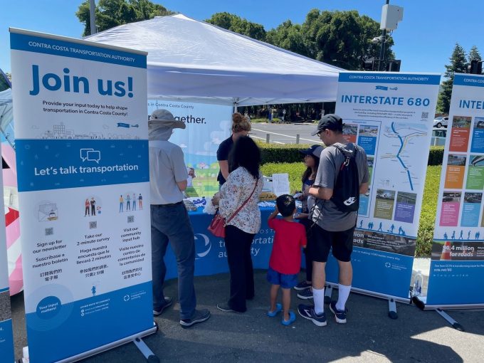People gathered at an outdoor Contra Costa Transportation Authority booth with informational banners about transportation and Interstate 680 projects.